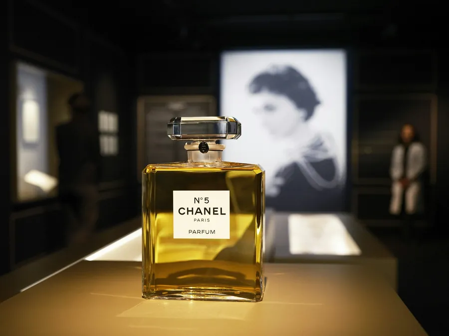 Flakon CHANEL N°5 beleuchtet auf einem Sockel, dahinter ein Schwarzweißporträt von Gabrielle Chanel